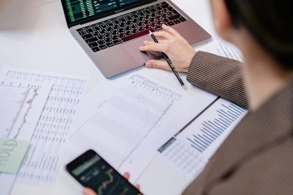 A business professional analyzing stock charts on a laptop and smartphone at the office.